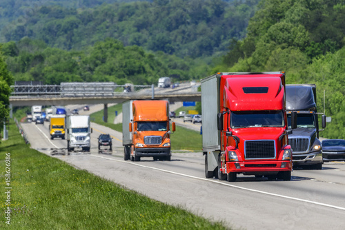 Flow of semis lead the way on a busy Tennessee highway. Heat waves rising from the pavement give a nice effect to vehicles and forest behind lead trucks. Copy space across top and bottom of image.