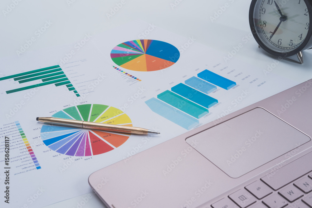 Colorful charts and spreadsheet on desk with laptop and pen Colorful charts and spreadsheet on desk with laptop and pen
