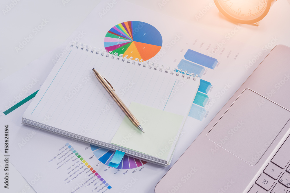 Colorful charts and spreadsheet on desk with laptop and pen Colorful charts and spreadsheet on desk with laptop and pen