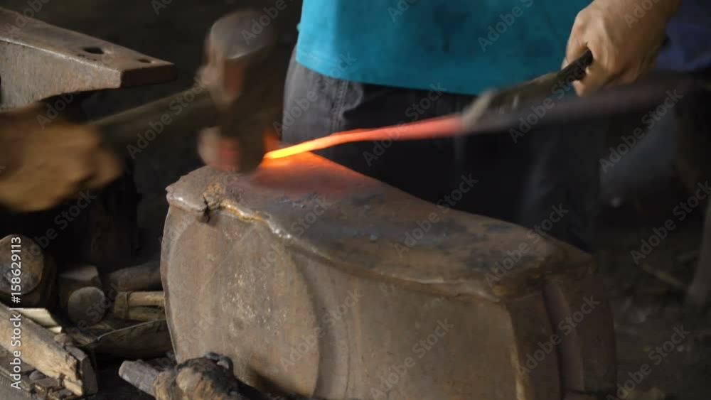 Blacksmith working metal with hammer on the anvil in the forge. hammer forging hot iron at anvil. Blacksmiths make machete. Hands of the smith by the work. 4K video, Philippines.