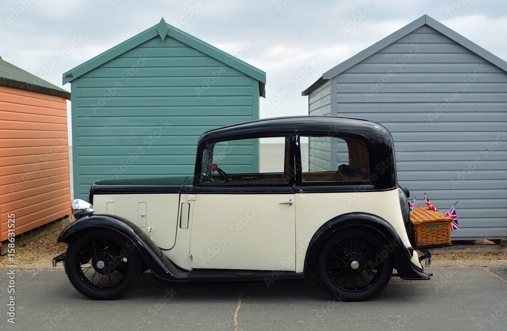 Vintage Cream and Black Austin Seven Motor Car with basket Parked on Seafront Promenade in front of beach huts.