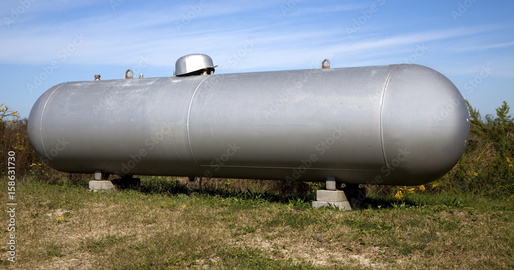 Silver industrial propane tank in field under blue sky. Silver industrial propane tank in field under blue sky.