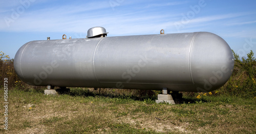 Silver industrial propane tank in field under blue sky.