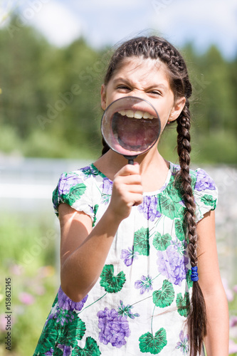 Girl holds magnifying glass and showing opened mouth with teeth