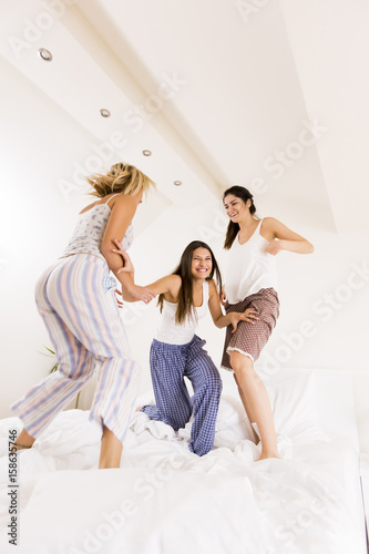 Three pretty young happy women jumping in the bed