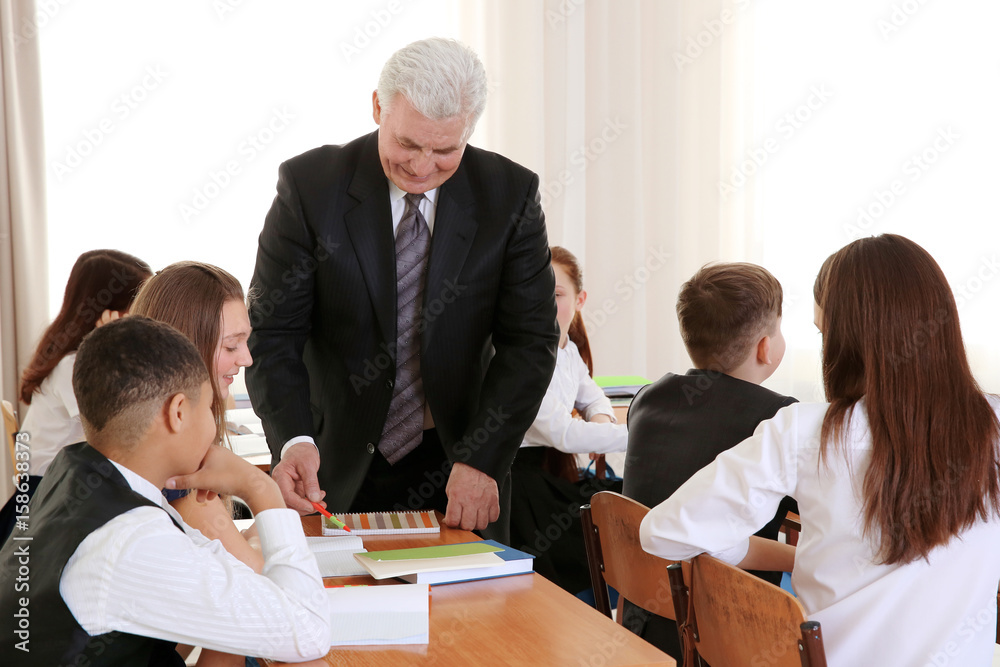 Fototapeta premium Senior teacher explaining exercise to pupils in classroom