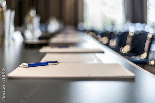 Canvas Print Close up of dark conference table water glasses pens, paper sheets and blurry wi