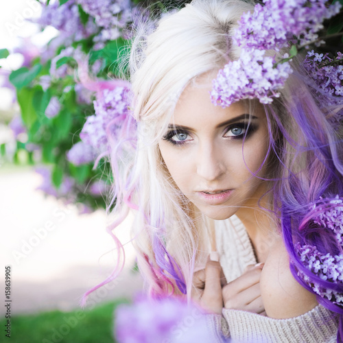 close-up portrait of a beautiful sexy young blonde girl hipster with lilac and pink hair on the background of blooming lilacs, posing