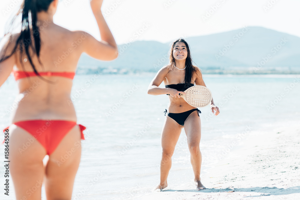 Couple of women millennials playing rachet on the seashore - summer activities, sportive, beach game concept
