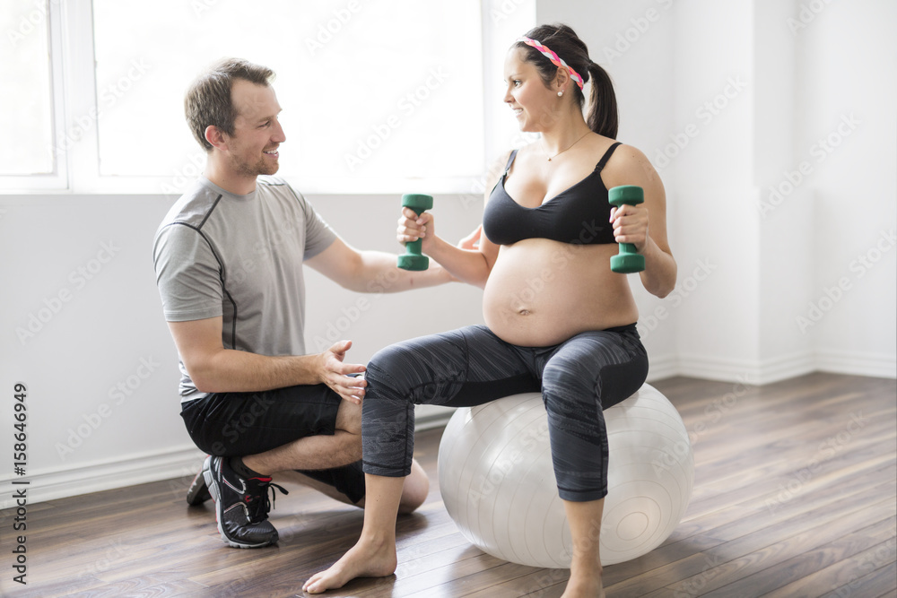 Pregnant woman working out with dumbbells with personal trainer at the gym