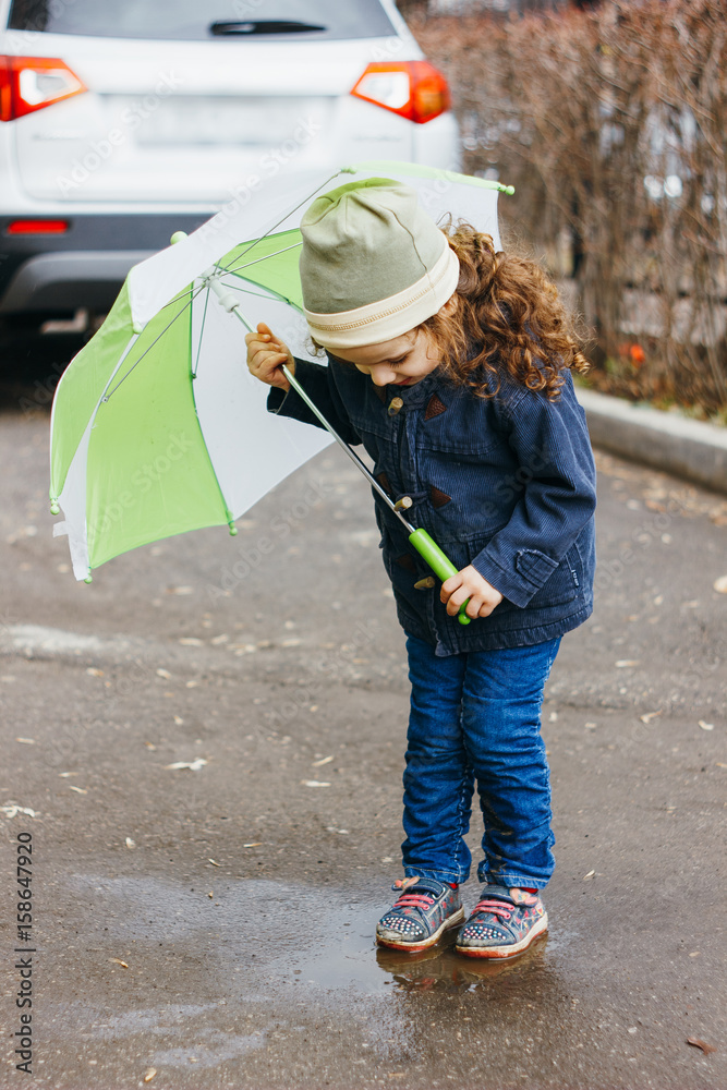 Little girl playting on the rainy street with green umbrella.