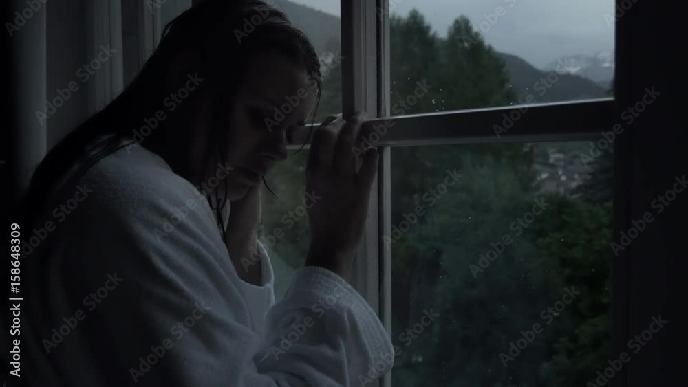 Sad lonely woman crying in front of window in mountains with rain dolly shot