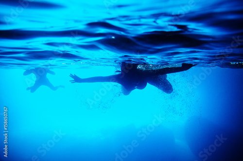 silhouette of people swim underwater