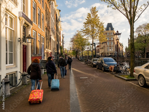 Canvas Print A group of tourists in Amsterdam with suitcases in the spring evening