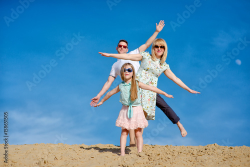 Beautiful happy family walking, running, jumping, having fun along the sand on the beach against the background blue sky in summer vacation