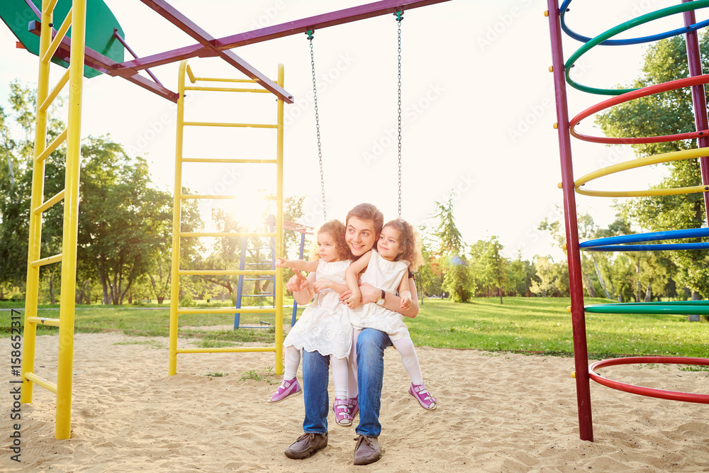 Father with children playing on a swing at the playground. Father with children playing on a swing at the playground.