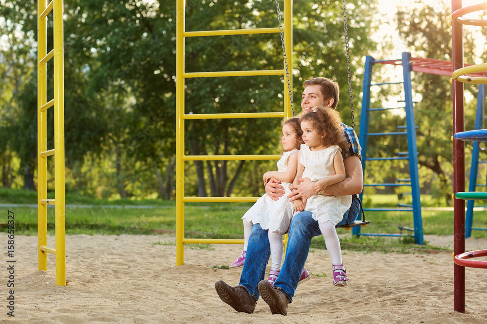 Father with children playing on a swing at the playground. Father with children playing on a swing at the playground.