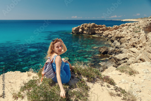 Beautiful young woman sitting at the edge of the rock against blue sea.