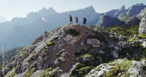 Aerial flight above people hiking along trail path in sunny day. Group of friends summer adventure journey in mountain nature outdoors. Travel exploring Alps, Dolomites, Italy. 4k drone forward video