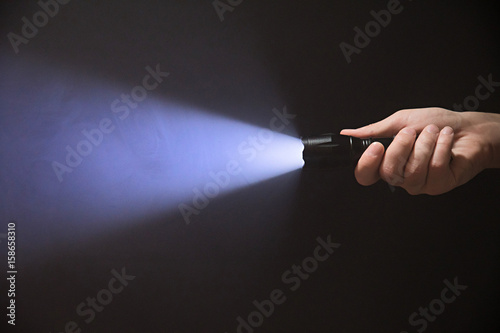 Male hand holding a led flashlight with blue beam on a black background, leaving the right side of the frame