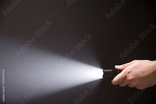 Male hand holding a led flashlight with white beam on a black background, leaving the right side of the frame