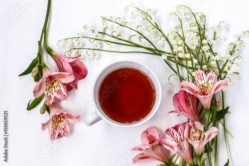 Cup of black tea with Lily of the valley and lilies on a white table