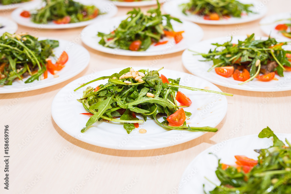 Many plates with fresh salad with chicken, tomatoes, nuts and mixed greens arugula, mesclun, mache on the table. Healthy food. Many plates with fresh salad with chicken, tomatoes, nuts and mixed greens arugula, mesclun, mache on the table. Healthy food.