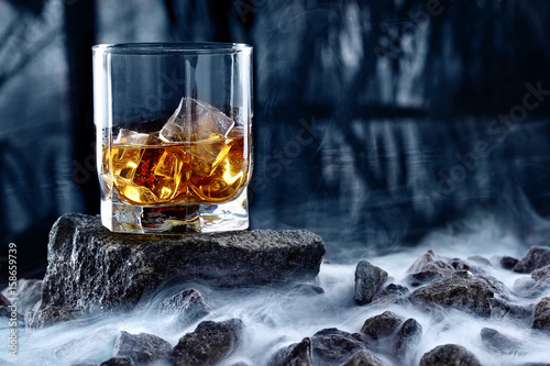 Glass of whiskey and ice.Creative photo glass of whiskey on stone with fog and cold background.Copy space.Advertising shot