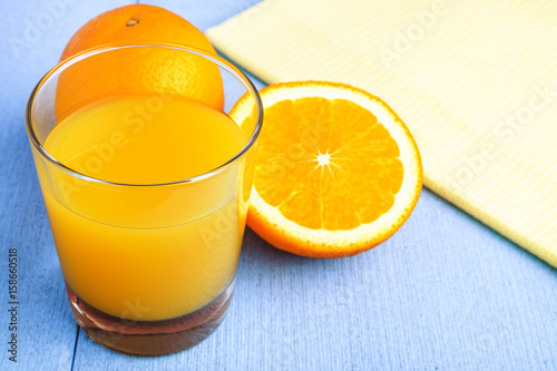 Fresh orange juice in the glass next to the orange slices on blue wooden table