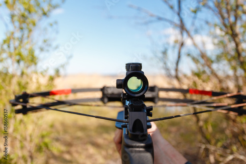 Fotografija A crossbow with a sight to aim in first person on the background of the lake
