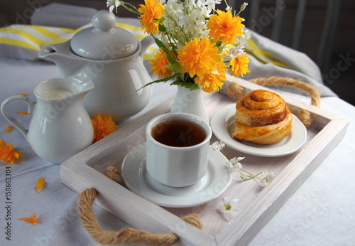 чашка чая со свежей булочкой и букетом цветов.завтрак в постель