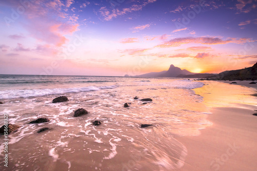 Romantic atmosphere in peaceful Sunset at Bai nhat beach Condao island-Vietnam. Taking with long exposure in the evening smooth wavy motion by Big rocks near shoreline, pink horizon with sun rays.