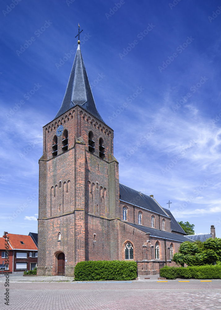 Gothic Saint-Servatius church in Ravels, Belgium, against a blue sky with dramatic clouds.