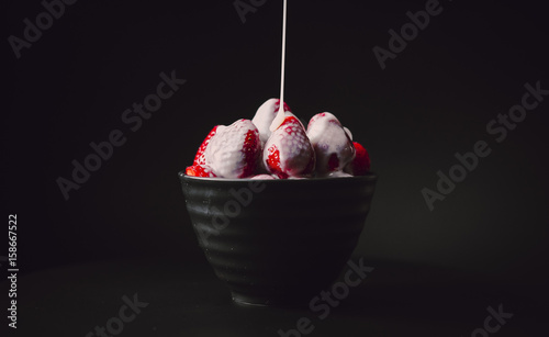 Strawberries with condensed milk in a black plate on a dark background.