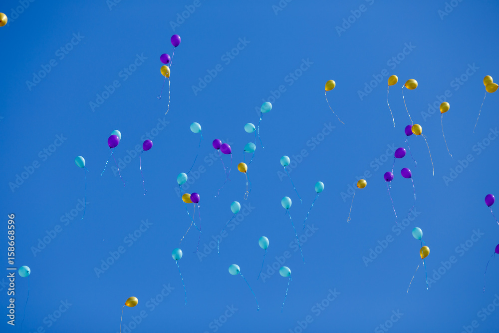 Naklejka premium Group of floating yellow, blue and violet balloons in the blue cloudless sky