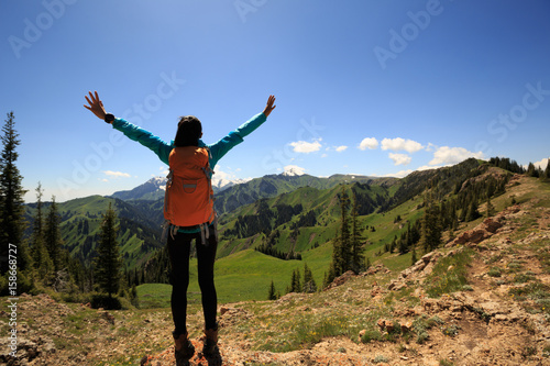 Cheering young woman hiker open arms on mountain top .