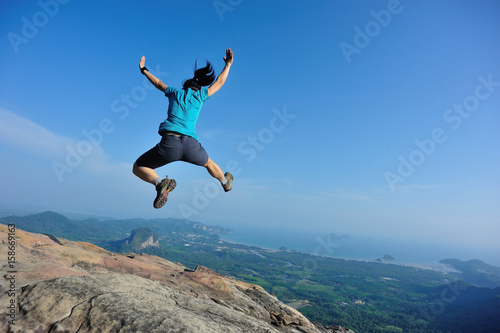 successful woman jumping on rocky mountain peak