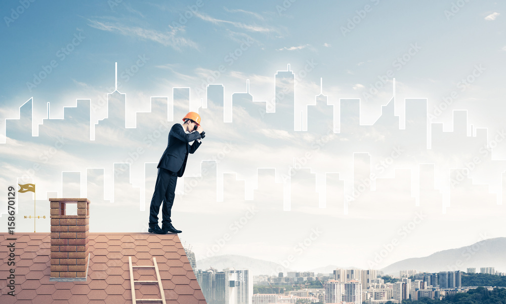 Engineer man standing on roof and looking in binoculars. Mixed m Engineer man standing on roof and looking in binoculars. Mixed m