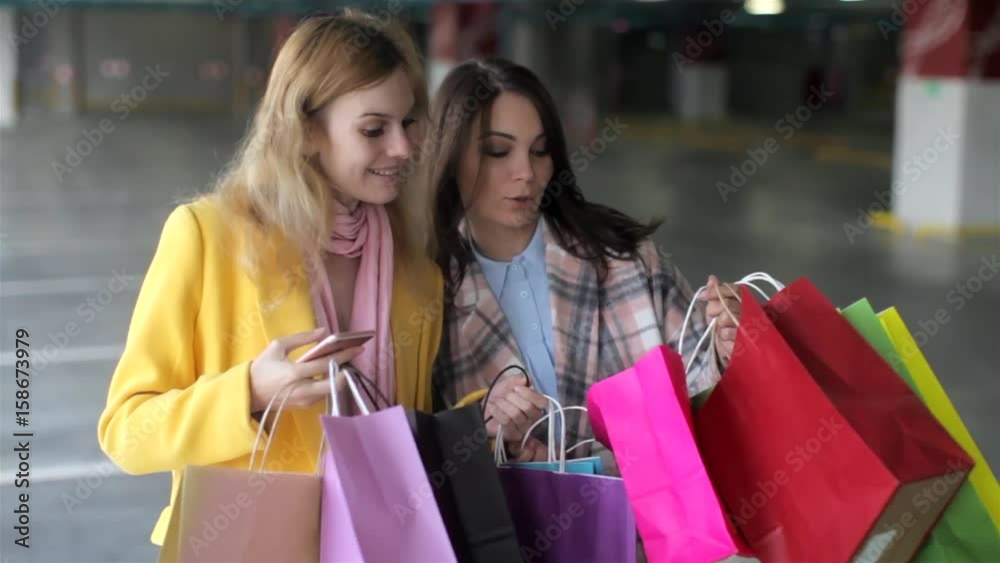 Two Happy Girls With a Bunch of Shopping Packages in the Shopping Center Parking Two Happy Girls With a Bunch of Shopping Packages in the Shopping Center Parking
