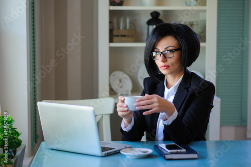 business lady with glasses dressed in black suit working on a laptop