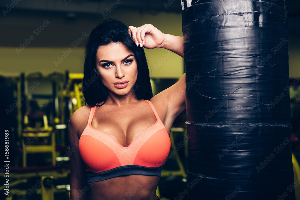 Sexy fitness model woman posing near punching bag in sport gym.