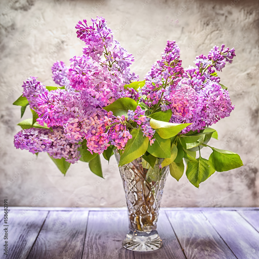 A bouquet of lilac in a crystal vase on the background of a textured wall