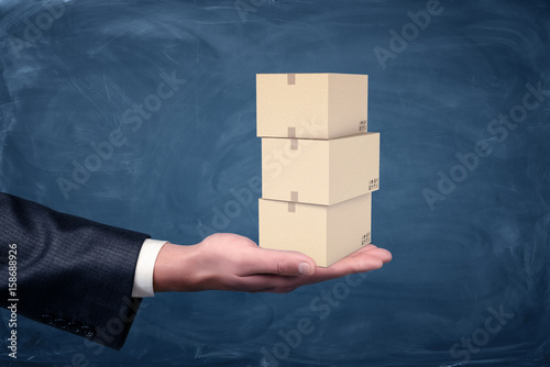 Photography A businessman's hand holding a set of small three cardboard boxes palm up on chalkboard background
