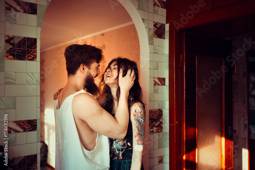 Loving couple lying in bed together. Handsome young hipster with beard and attractive woman resting at home while kissing and cuddling.