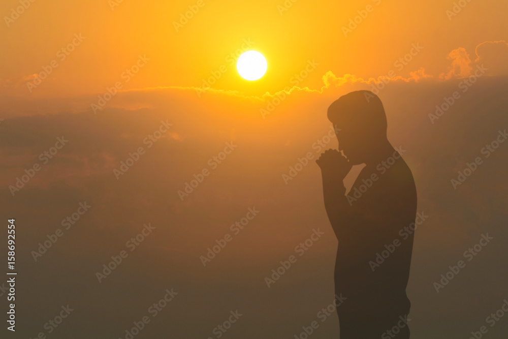 Man praying on cliff against sunset background