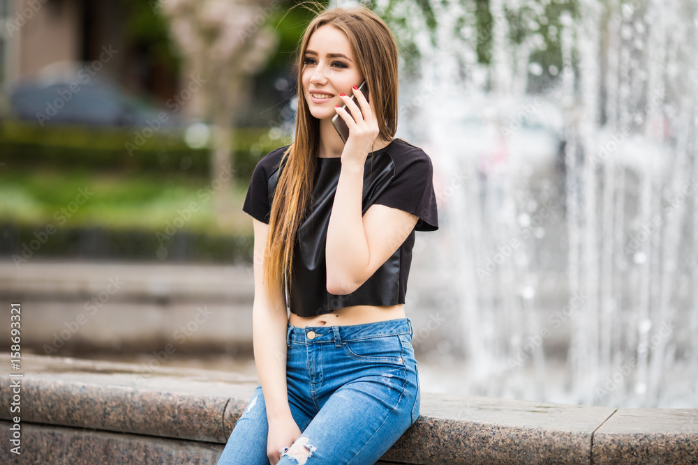 Young girl speak on mobile phone outdoors near fountain