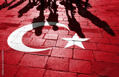 Shadows of group of people walking through the sunny streets with painted Turkey flag on the floor.