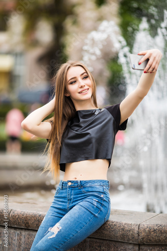 Young happy woman make selfie on the street of old town with fountain in background.