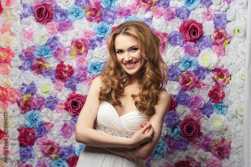 Beautiful woman smiling, wearing a wedding dress on a background of flowers. Emotion shyness © alexsfoto
