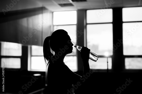Resting time. Silhouette of sporty girl drink water. Photo of fitness model. Health concept. photo